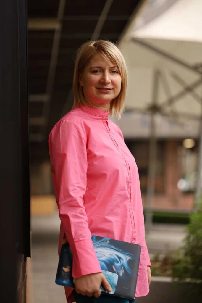 Nika Mak performance mindset coach in a pink shirt outside with a laptop 